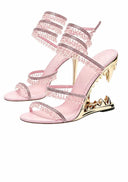 A pair of Dolly Bae pink strappy high-heeled sandals decorated with rhinestones and gold spikes on the heel, shown against a white background with the Dolly Bae logo above.