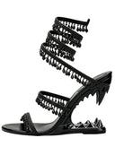 A single black strappy sandal with a high heel, featuring a spiral wraparound strap adorned with dangling teardrop charms, a pointed stiletto heel with spiked detailing, and a flat toe strap embellished with rhinestones.
