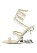 A single high-heeled sandal with a metallic silver wedge heel featuring a jagged spike design, decorated with multiple layers of pearl-embellished wraparound straps on a white background.