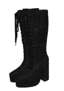 A pair of black knee-high lace-up boots with a chunky block heel, platform sole, and intricate gothic-style embossed patterns on the shaft.