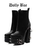 A pair of black leather platform ankle boots with high studded platform soles, chunky block heels, and silver chain details on the heel, shown against a white background with the 'Dolly Bae' brand name printed at the top.