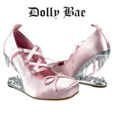A pair of light pink satin high-heeled shoes with lace-up front straps, bow details, and metallic silver spiked heels, shown on a white background with the text 'Dolly Bae' above.