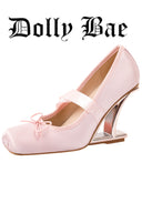 A light pink satin Mary Jane-style high heel shoe with a decorative bow on the toe and a metallic silver wedge heel, shown on a plain white background with the brand name 'Dolly Bae' printed above.