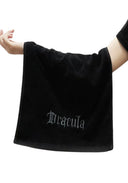 A black towel held up by a person's arms against a white background, featuring the word 'Dracula' embroidered in a gothic white font near the bottom.