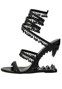 A single black strappy sandal with a high heel, featuring a spiral wraparound strap adorned with dangling teardrop charms, a pointed stiletto heel with spiked detailing, and a flat toe strap embellished with rhinestones.