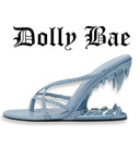 A light blue strappy sandal with braided straps and a shark-tooth-inspired heel, shown on a white background with the text 'Dolly Bae' above it.