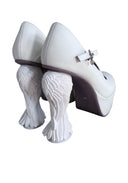 A pair of white Mary Jane style high heels with sculptural, textured white heels and dark brown soles, shown from a rear three-quarter angle on a white background.