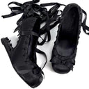 A pair of black satin ballet flats with decorative ruffles and long dangling ribbon laces, photographed on a plain white background.