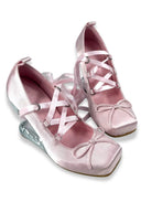 A pair of light pink satin wedge shoes with criss-cross lace-up straps, bow details on the toes, and clear plastic wedge heels, shown against a plain white background.