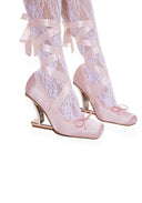 A pair of light pink satin high-heeled shoes with lace up straps and bows, worn with white lace thigh-high stockings, shown against a plain white background.