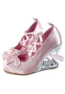 A pair of light pink satin high-heeled shoes with bow details on the toes and crisscrossing ribbon straps, featuring a metallic silver heel.