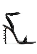 A single black patent leather stiletto sandal with a pointed toe, studded ankle strap, and spiked heel, shown from a side profile on a white background.