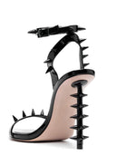 A single black patent leather studded high-heeled sandal with an ankle strap and a pale blush pink footbed, shown from a side profile on a white background.