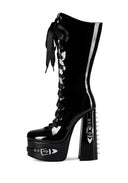 A single black patent leather knee-high boot with a high platform sole, a chunky block heel with metal spikes, and a black ribbon bow at the ankle, shown against a plain white background.
