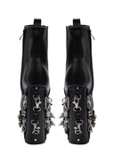 A pair of black leather ankle boots with dramatic silver metal hardware, spikes, and chain-link details on the stacked block heels, shown from the back against a white background.