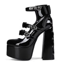 A single black patent leather high-heeled shoe with a platform sole, chunky block heel, ankle strap, and decorative silver-tone heart-shaped hardware, shown on a plain white background.