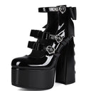 A pair of glossy black patent leather platform high-heeled shoes with double ankle straps, silver buckle details, and a large black bow on the back heel, shown against a plain white background.
