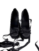 A pair of black satin high-heeled shoes with long dangling ribbon straps, displayed on a white background with the text 'Dolly Bae' above them.