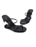 A pair of black patent leather mule sandals with a unique claw-heel design, displayed on a white background with the brand name 'Dolly Bae' printed in a gothic font at the top.