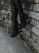 Person wearing black shoes and stockings against a stone wall.