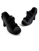 A pair of black gothic-style high heels with ruffled straps and bows, displayed on a clean white background with the brand name 'Dolly Bae' printed in a gothic font above them.