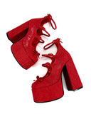 A pair of red platform high heels with lace-up ankle straps and block heels, shown on a plain white background with the text 'Dolly Bae' above them.