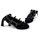 A pair of black gothic-style low-heel shoes with velvet texture, ruffled trim, silver chain details, and buckle straps, displayed on a white background with the brand name 'Dolly Bae' printed above.