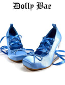 A pair of light blue satin high-heeled shoes with matching blue ribbon laces, displayed on a white background with the text 'Dolly Bae' printed above.