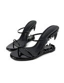 A pair of black patent leather strappy heeled sandals with spiked heels and a matching spiked platform sole, shown on a white background with the brand name 'Dolly Bae' printed above.