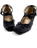 A pair of black satin Mary Jane shoes with ankle straps and bow details, displayed on a white background with the brand name 'Dolly Bae' printed above.