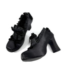 A pair of black lace-up ankle boots with block heels and ruffled details, shown on a plain white background with the brand name 'Dolly Bae' printed above in a gothic font.