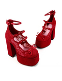 A pair of red lace and velvet platform high-heeled shoes with ankle straps and bow details, displayed on a white background with the brand name 'Dolly Bae' printed above.
