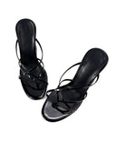 A pair of black patent leather strappy high-heeled sandals with a square toe, displayed on a clean white background with the brand name 'Dolly Bae' printed in a black gothic font at the top.