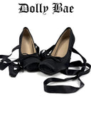 A pair of black satin high-heeled shoes with long dangling ribbon straps, displayed on a white background with the text 'Dolly Bae' above them.