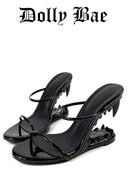 A pair of glossy black strappy high-heeled sandals with sharp claw-like heel details, shown on a plain white background with the brand name 'Dolly Bae' printed above.