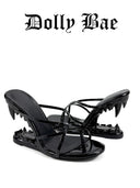 A pair of black patent leather mule sandals with high heels shaped like open mouths and sharp teeth along the bottom edge, shown on a white background with the text 'Dolly Bae' above them.