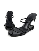 A pair of black patent leather strappy mule sandals with a low block heel, displayed on a white background with the brand name 'Dolly Bae' printed in a black gothic font at the top.