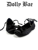 A pair of black satin ballet flats with bow details and studded straps, displayed on a white background with the brand name 'Dolly Bae' printed above in a gothic font.