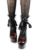 A pair of gothic platform ankle boots with dark brown glossy leather and black lace-up details, styled with patterned black tights. The brand name 'Dolly Bae' is printed in a black gothic font at the bottom of the image.