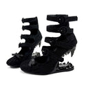 A pair of black strappy high-heeled shoes with spiked heels and decorative bows, shown on a plain white background with the text 'Dolly Bae' above them.