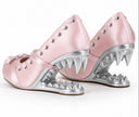 A pair of pink satin Mary Jane-style shoes with metallic silver spikes forming shark-like teeth along the sole, set against a plain white background.